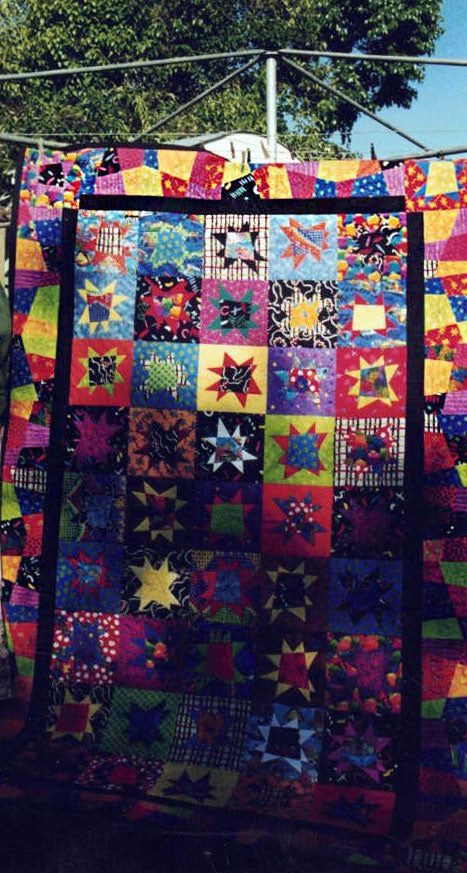 A close up of a quilt in a scanned photograph. Brightly coloured stars with a black border