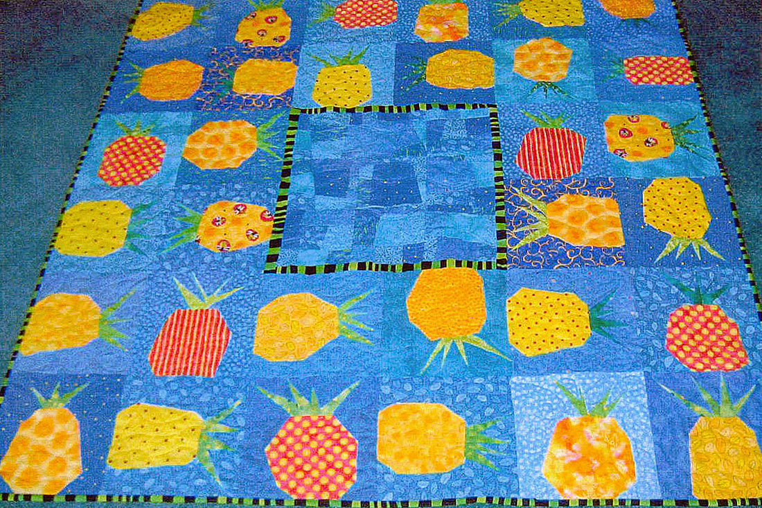 A quilt laying on a blue carpet. The quilt is square with modern, wonky pineapple blocks around the edges.