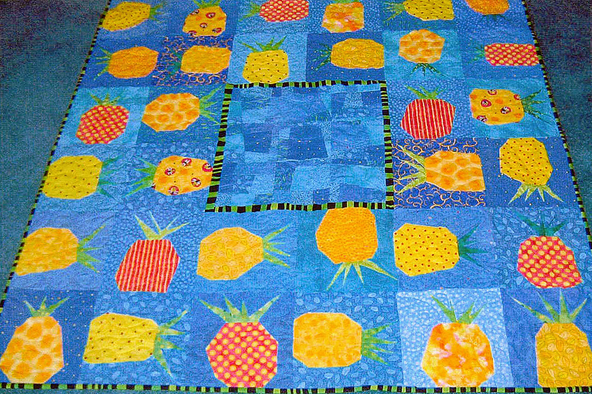 A quilt laying on a blue carpet. The quilt is square with modern, wonky pineapple blocks around the edges.