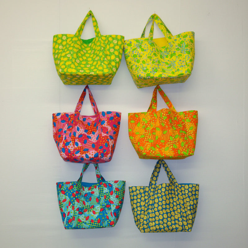 Six colorful patterned bags hanging on a white wall.