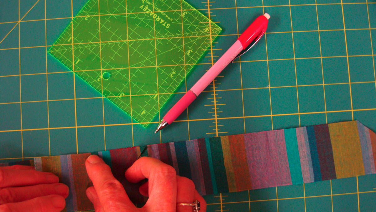 Colorful fabric strip on a cutting mat with a ruler and pen