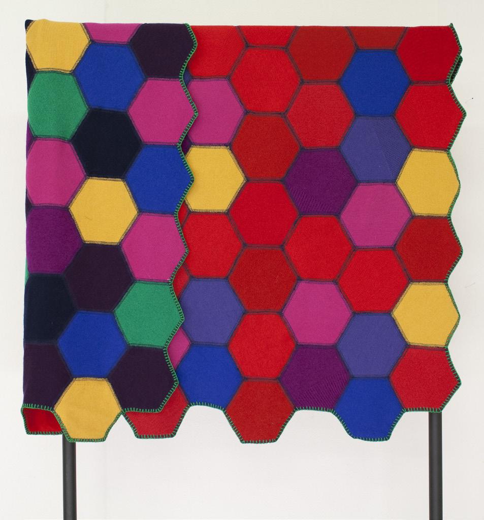 Colorful hexagonal patterned woollen quilt on a stand against a white background