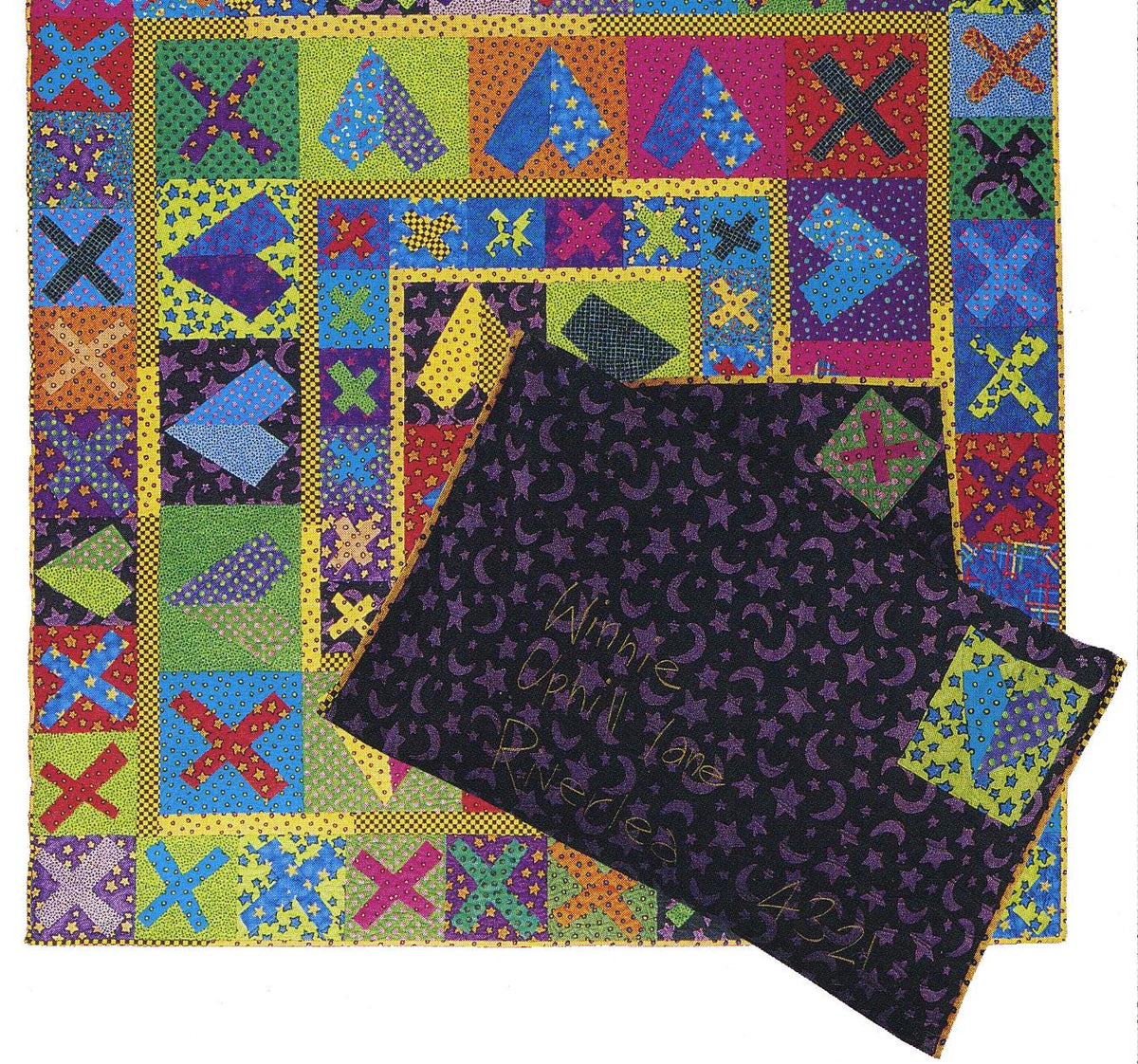 Colorful patchwork quilt with a folded black fabric envelope featuring embroidery text on a white background.
