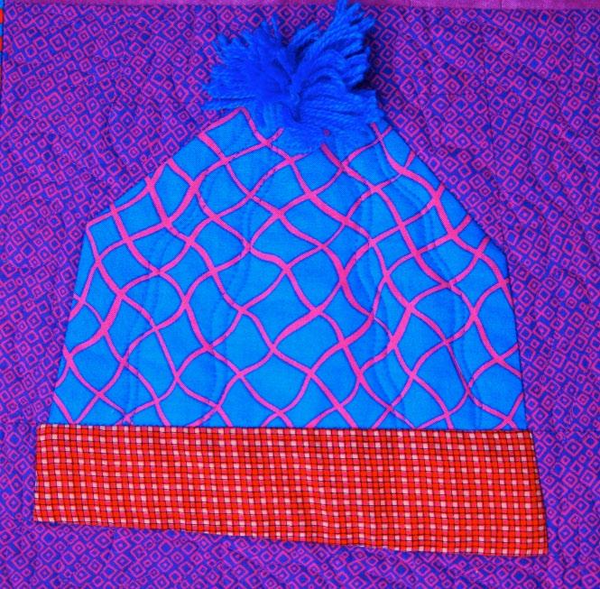Blue knit beanie with pink pattern and red checkered band on a purple patterned background